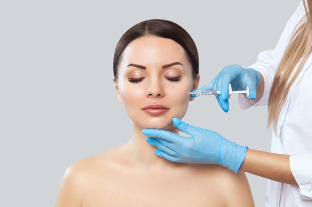 Medical aesthetic professional injecting dermal filler into woman’s cheekbone